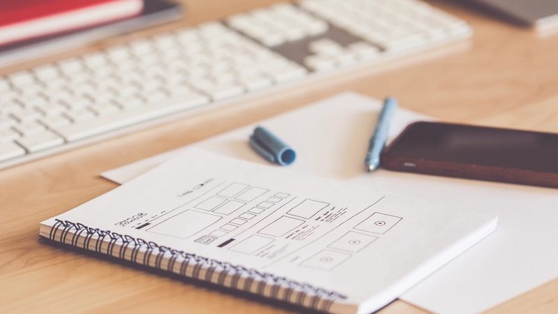 A hand-drawn website wireframe on a notepad beside a keyboard