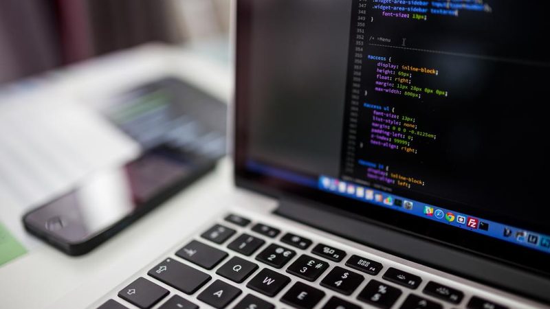 Code on a laptop screen beside a phone